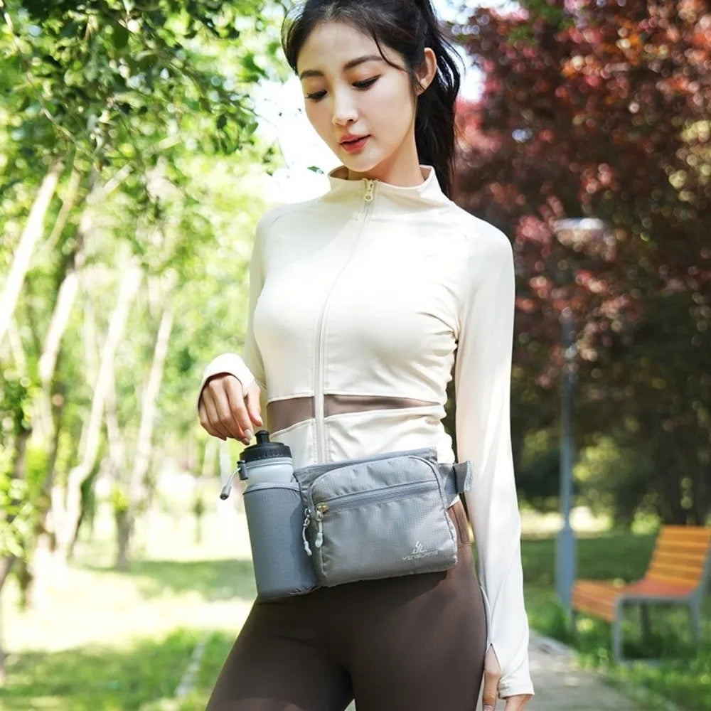 A woman wearing a beige long-sleeved top and brown pants holds a gray waterproof invisible waist pack.
