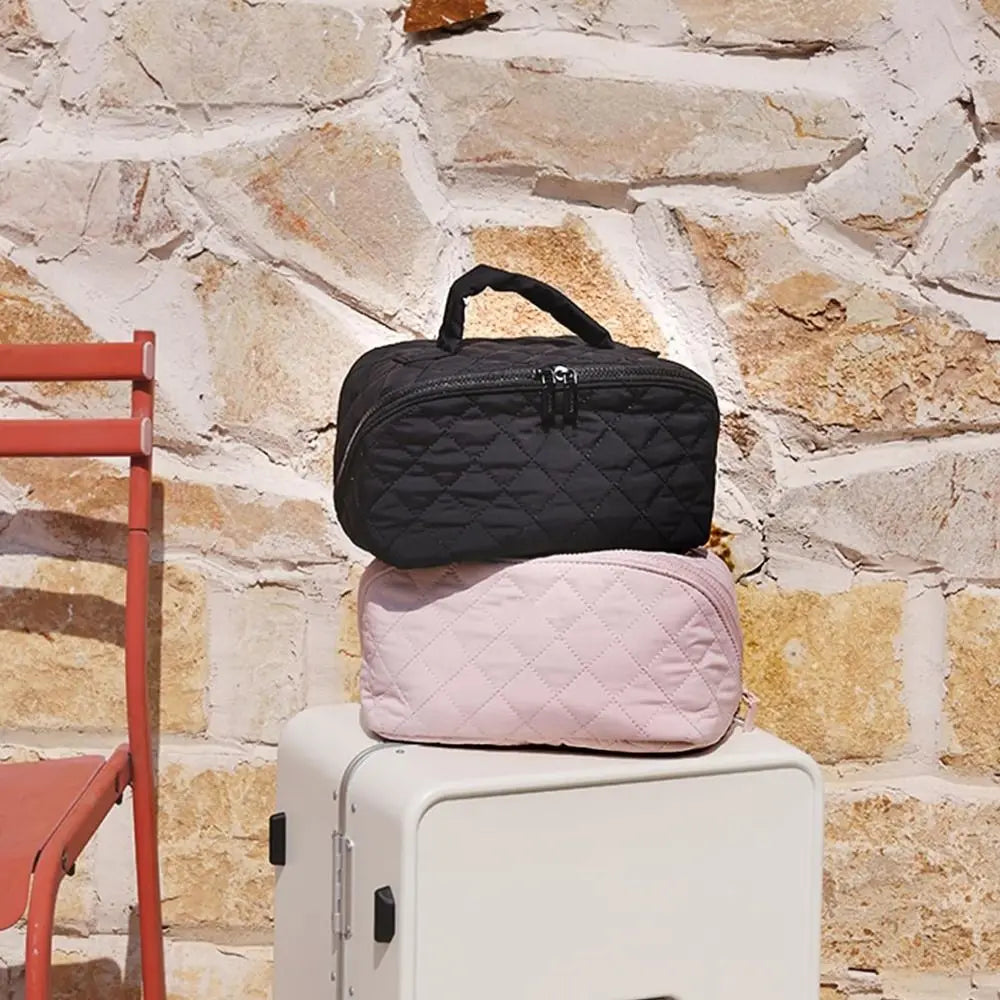 A black quilted makeup organizer bag resting on a white suitcase against a stone wall.