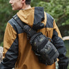A man wearing a tan and black waterproof jacket carrying a tactical chest bag while outdoors.