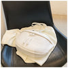 A cream-colored PU leather crossbody saddle bag with a white chain strap resting on a black leather chair.