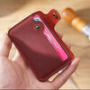 Una mano sostiene un elegante porta tarjetas de cuero genuino con una tarjeta rosa visible sobre una superficie de madera.
