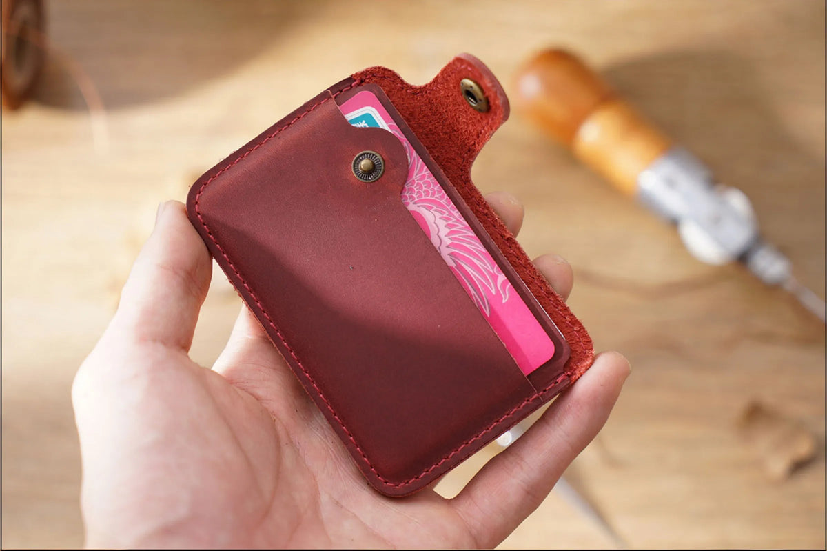 Una mano sostiene un elegante porta tarjetas de cuero genuino con una tarjeta rosa visible sobre una superficie de madera.