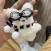 A fluffy white rabbit plush toy wearing black glasses and a black patterned collar is held in a hand.