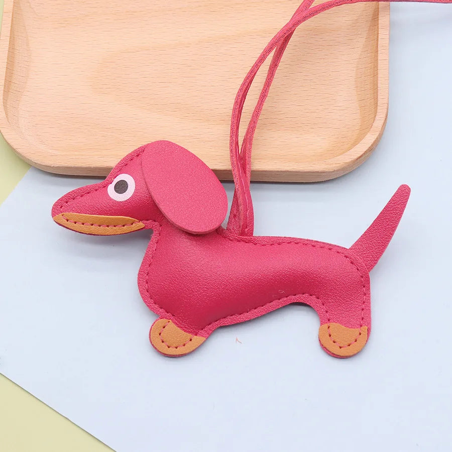 A pink leather dachshund keychain charm with an attached strap resting on a light wooden tray.