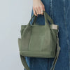 A woman holds a olive green canvas crossbody bag with a tan strap against a light gray background.