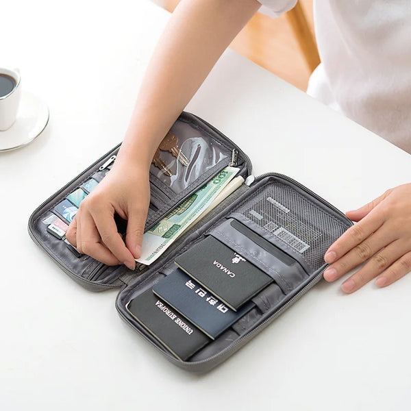 A hand is opening a multi-pocket waterproof travel document organizer containing various currency and cards.