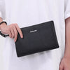 Schwarze Kunstleder-Herrengeldtasche wird von einer Hand gegen ein weißes Hemd gehalten.