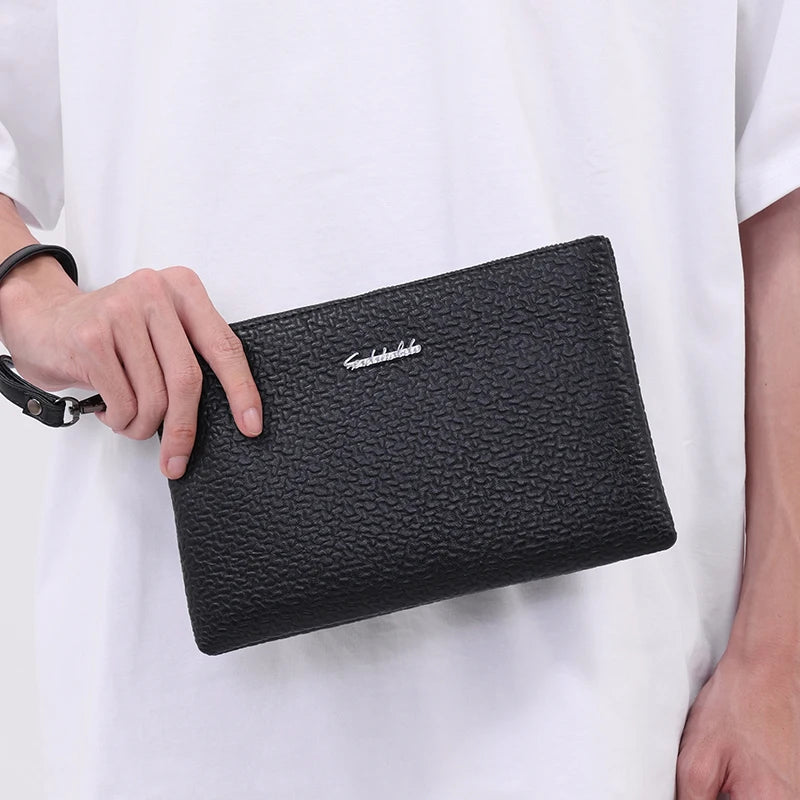 Schwarze Kunstleder-Herrengeldtasche wird von einer Hand gegen ein weißes Hemd gehalten.