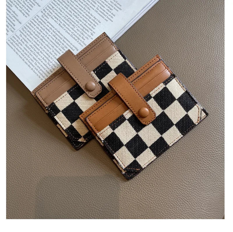 A checkered brown and black PU leather mini card wallet with leather straps resting on a piece of paper.
