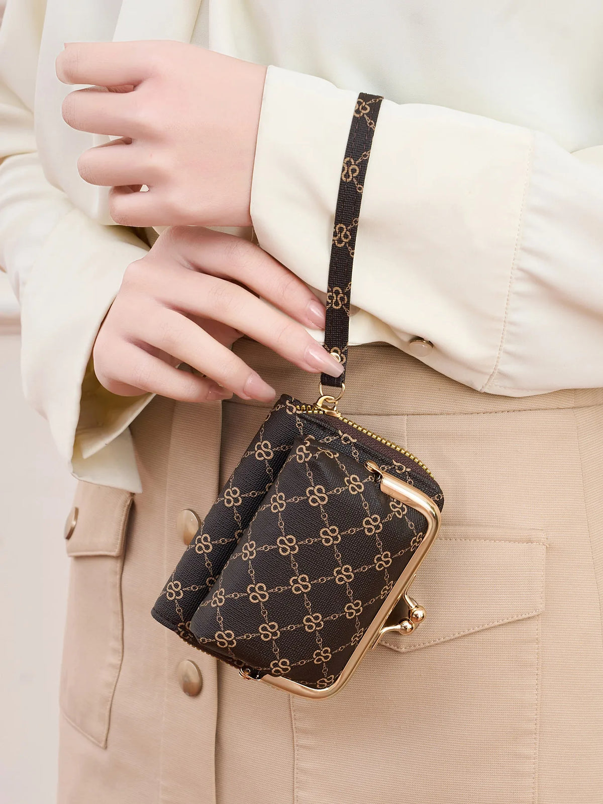 A close-up of a brown patterned accordion card holder wallet with gold accents held by a person wearing a cream blouse.
