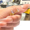 A hand holds a set of gold-toned stainless steel ear stud earrings featuring pink and clear gemstones.