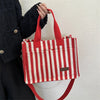 Une femme tient un sac bandoulière à toile rayé rouge et blanc sur un fond clair.