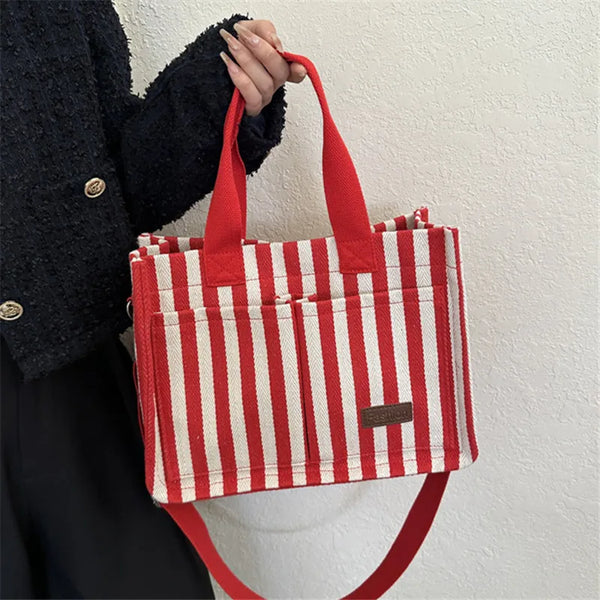 A woman holds a red and white striped canvas crossbody bag against a light background.