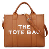 Sac cabas en cuir tan avec une sangle marron et du texte blanc indiquant THE TOTE BAG.