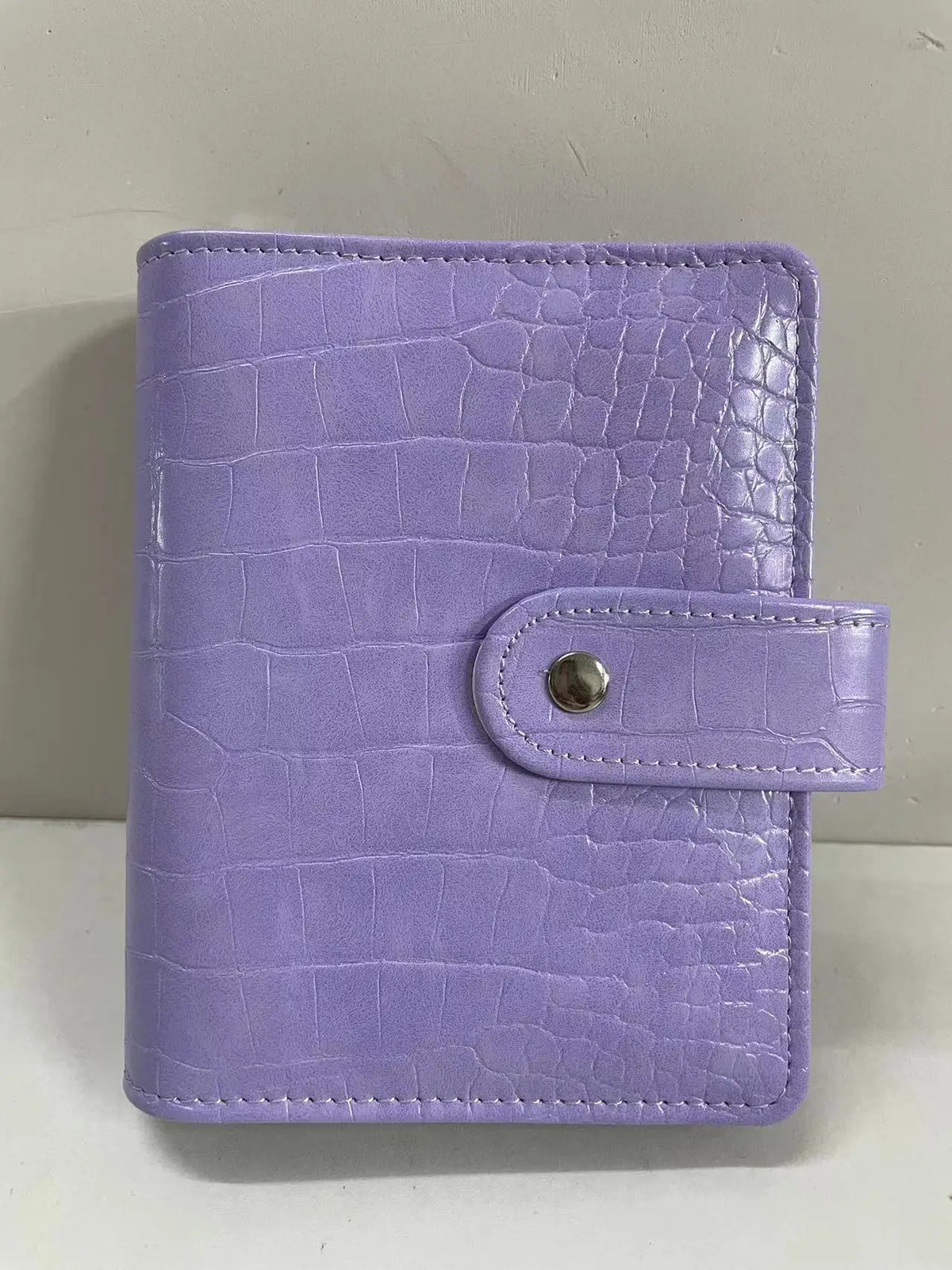 A purple crocodile leather ring binder notebook with a silver snap closure.