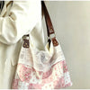 A light pink and white floral patchwork shoulder bag with a sheer lace overlay and brown leather strap.