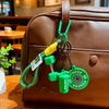 A green fitness keychain charm with a dumbbell and kettlebell is attached to a brown leather handbag.