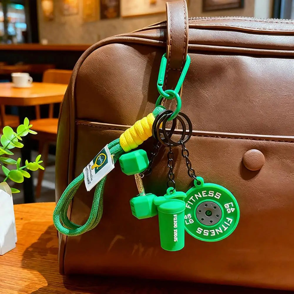 A green fitness keychain charm with a dumbbell and kettlebell is attached to a brown leather handbag.