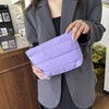 A woman holds a purple quilted cosmetic travel bag in her hand against a gray blazer.