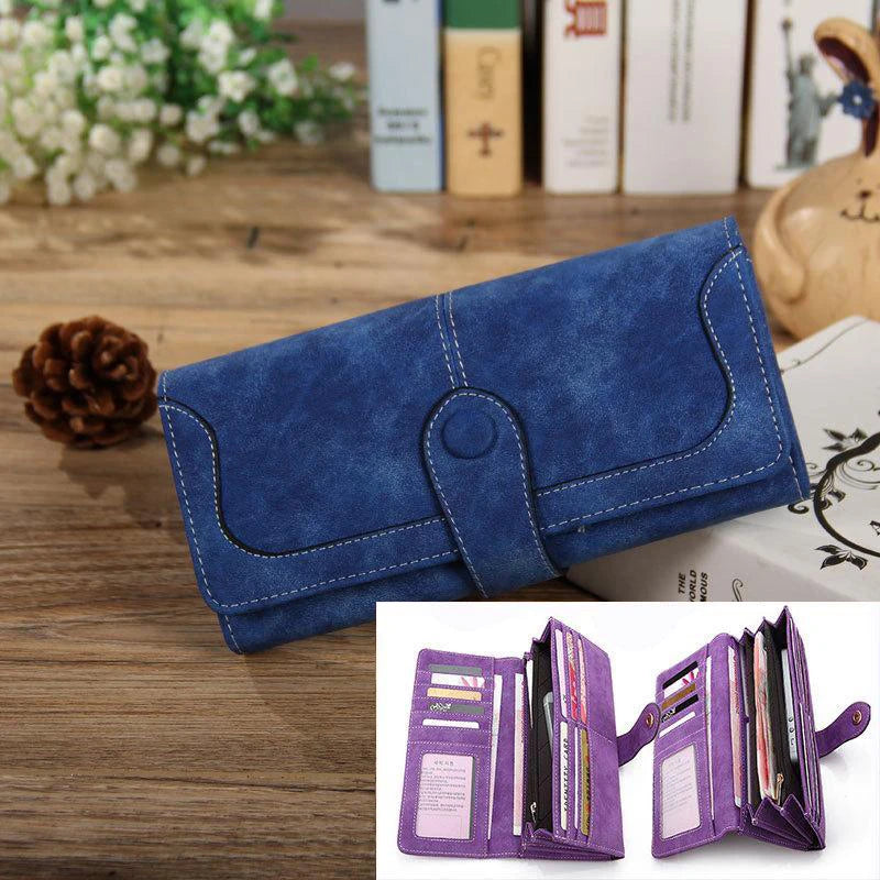A dark blue suede clutch wallet with a leather strap and RFID protection features is displayed on a wooden surface.
