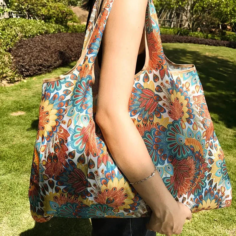 A person holds a colorful patterned fabric shopping tote bag outdoors on a grassy lawn.