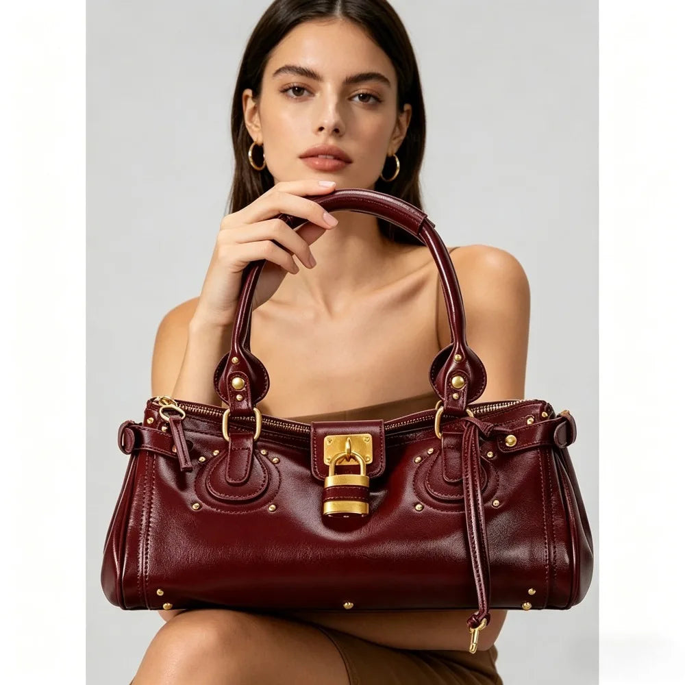 A woman holds a maroon vegan leather tote bag with gold hardware against a light gray background.