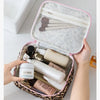 A hand opens a leopard print large capacity waterproof travel makeup organizer bag revealing various cosmetic bottles inside.