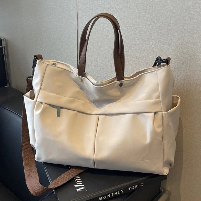 A beige lightweight nylon tote bag with brown leather handles and multiple internal pockets.