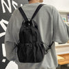 A person wearing a gray sweatshirt is shown from the back, carrying a black casual backpack with shoulder straps.