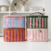 Cuatro bolsas de almacenamiento cosmético rayadas en rosa, azul, verde y naranja apiladas en un estante blanco.