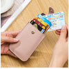 A hand holds a pink genuine leather slim card holder displaying various identification cards on a wooden surface.