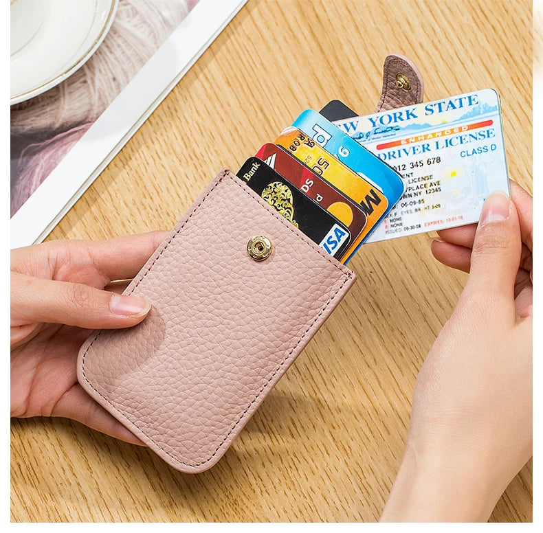 A hand holds a pink genuine leather slim card holder displaying various identification cards on a wooden surface.