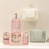 A pink waterproof hanging toiletry bag with a clear window and a light green cosmetic pouch is displayed on a white surface.