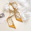 Un foulard pour les cheveux en soie élégant, motif floral or et blanc, présenté sur du papier de soie blanc froissé.