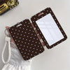 A dark brown card holder with a grid design and a white insert is being held by a hand, featuring a white cord lanyard.