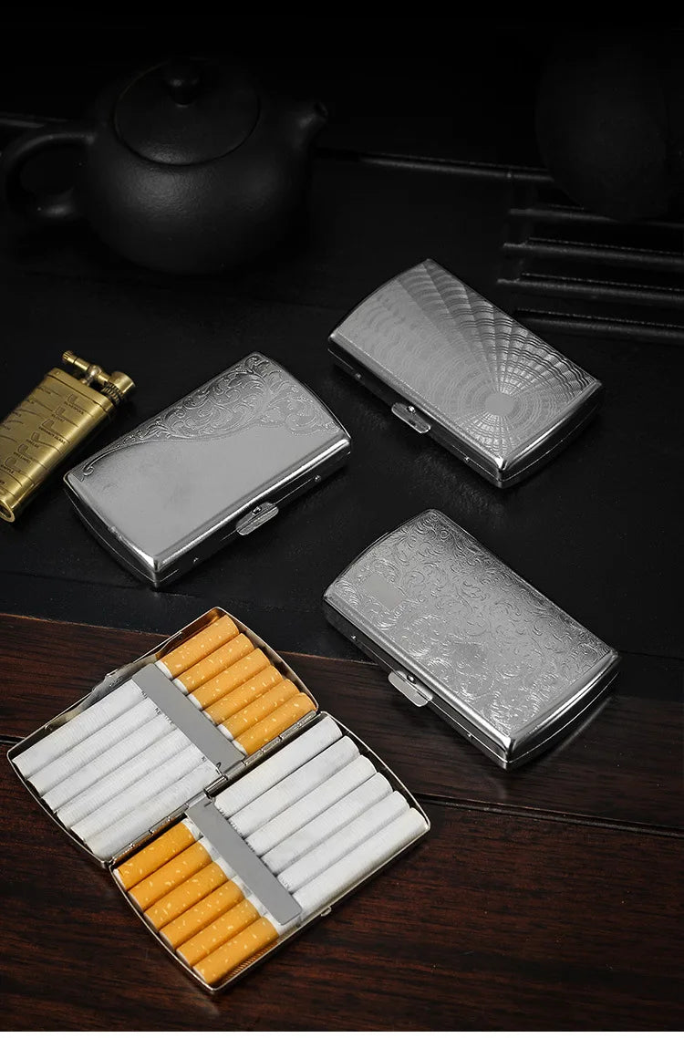 A set of compact metal cigarette cases, including a silver rectangular case and an open box containing 12 orange cigarettes.