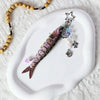 A purple and black simulation fish keychain with a silver star charm resting on a white ceramic plate.