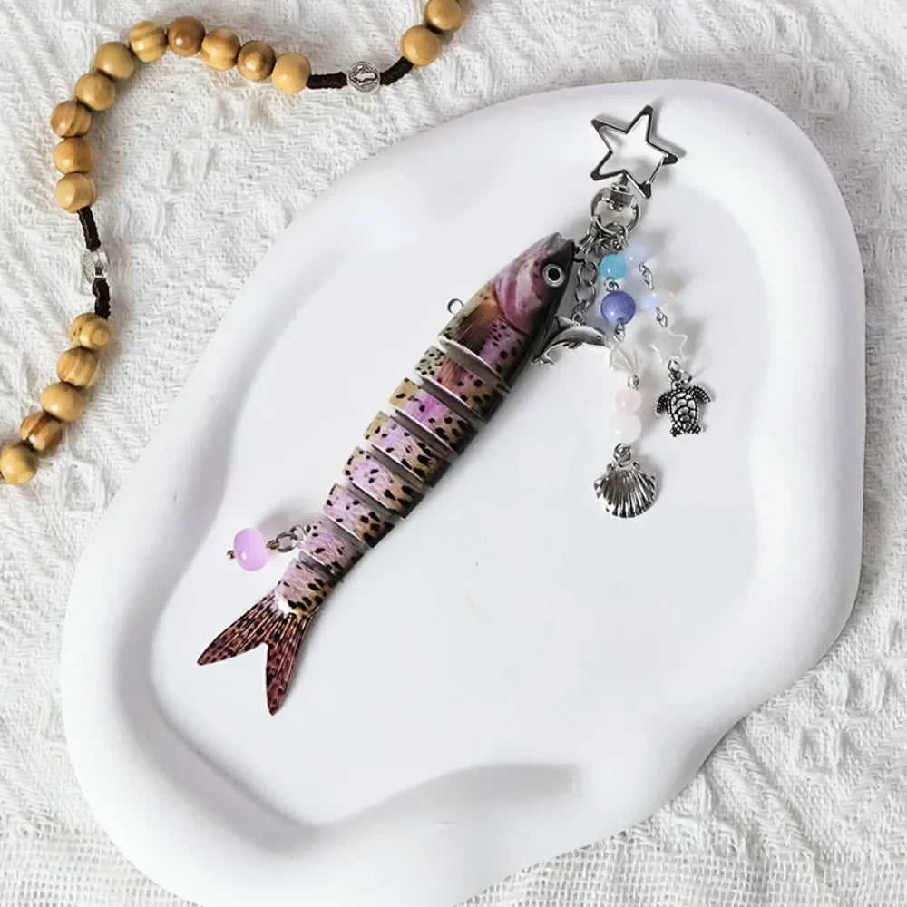 A purple and black simulation fish keychain with a silver star charm resting on a white ceramic plate.