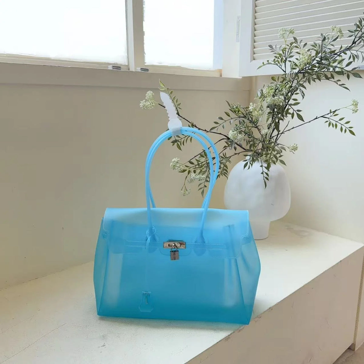 Helles blaues Sommer-Gelidertasche auf weißer Oberfläche neben einem Fenster mit Grün