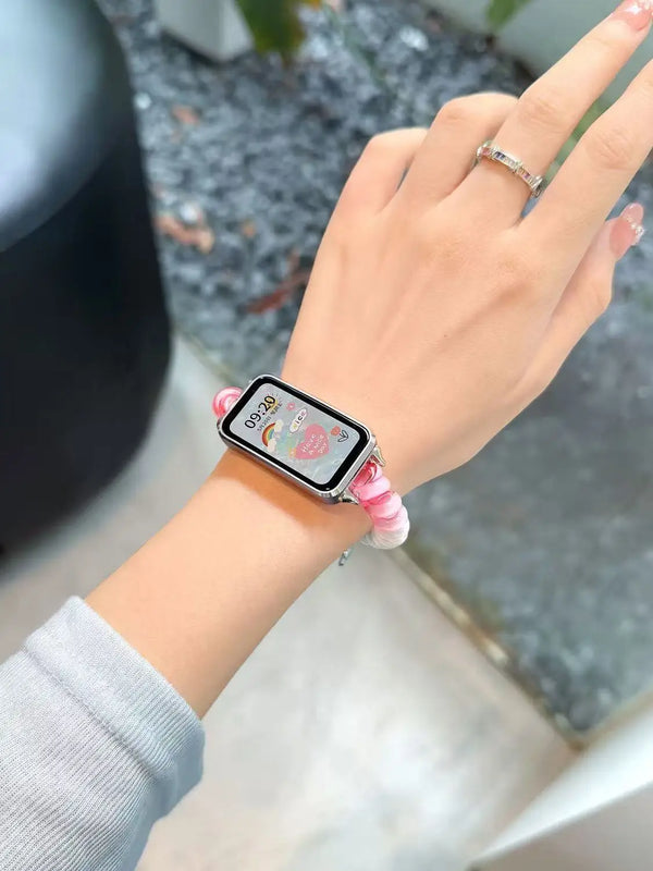 Une main portant une montre connectée avec un bracelet élastique rose sur une manche gris clair.