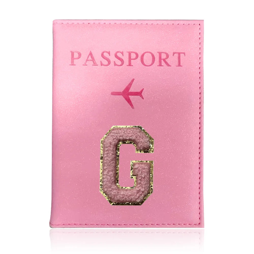 A pink leather passport holder with gold embossed letter G and a small airplane symbol.
