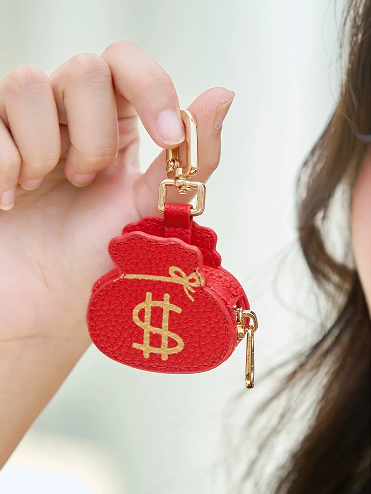 Una mano sostiene una cartera de monedas con forma de corazón y panda de cartón rojo con herrajes dorados.