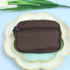 A dark brown nylon mini coin purse with a double zipper is placed on a light ceramic plate.