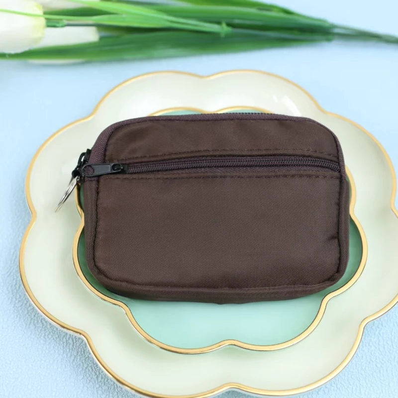 A dark brown nylon mini coin purse with a double zipper is placed on a light ceramic plate.