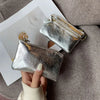 A silver metallic leather compact coin purse and key holder is shown being held against a gray fabric background.