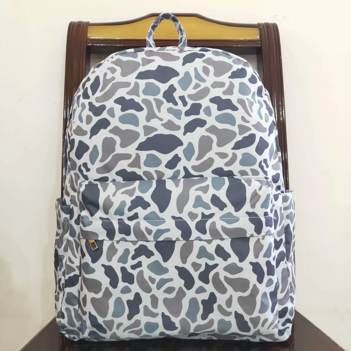 A gray and white camouflage patterned toddler backpack displayed on a wooden hanger.