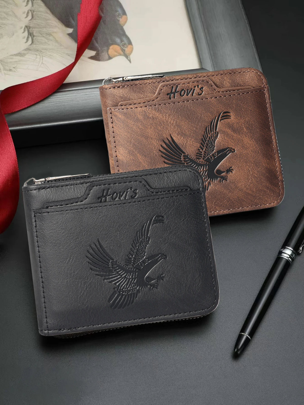 A set of brown and black embossed PU leather slim wallets and a pen displayed on a dark surface.
