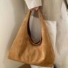 A tan suede shoulder tote bag carried by a person wearing light-colored pants and a jacket.