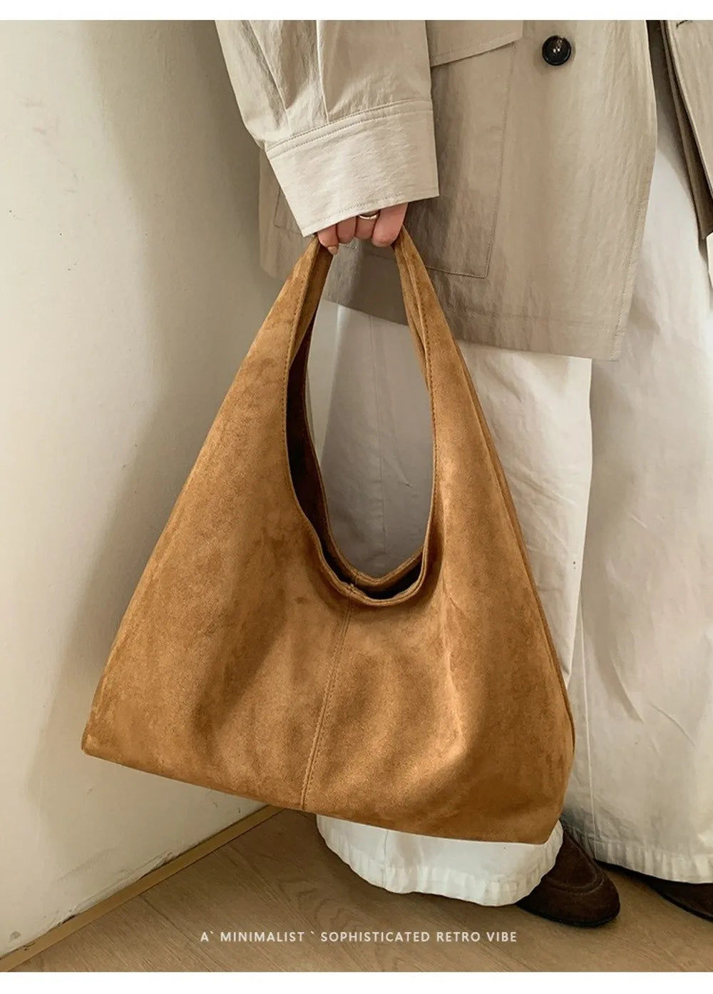 A tan suede shoulder tote bag carried by a person wearing light-colored pants and a jacket.