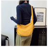 A woman wearing a navy blue sweater and olive pants holds a yellow canvas crossbody bag.